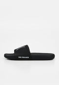 Schwarze Slide-Sandale mit breitem Riemen, der ein kleines erhabenes Logo und den Text "BORN FROM WATER" an der Seite zeigt.