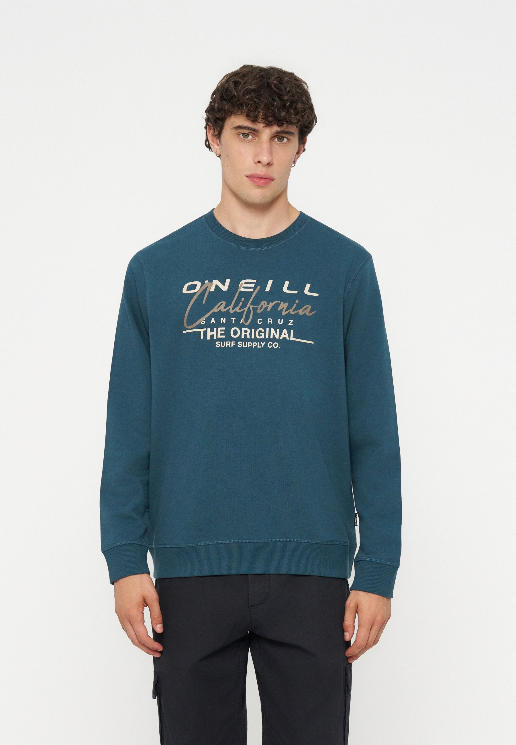 Junger Mann mit dunklem lockigem Haar, der ein türkisfarbenes Sweatshirt mit beigem Schriftzug „O'Neill California Santa Cruz Surf Supply Co.“ trägt.