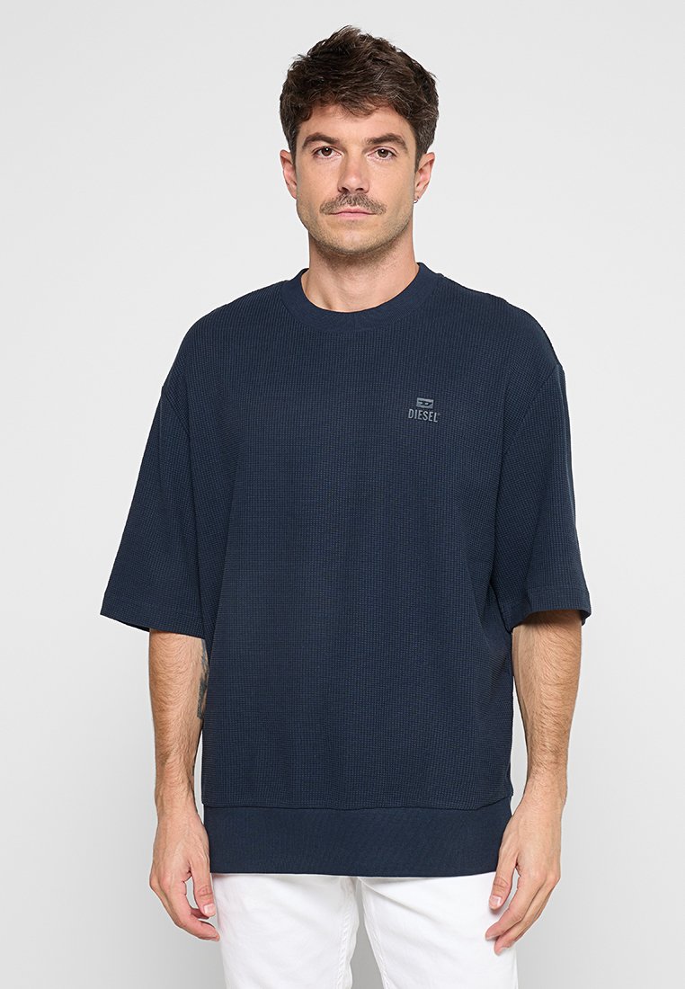 Navy-blaues T-Shirt mit kurzen Ärmeln und Rundhalsausschnitt aus strukturiertem Stoff, mit einem Logopatch auf der Brust und einem gerippten Saum am unteren Ende.