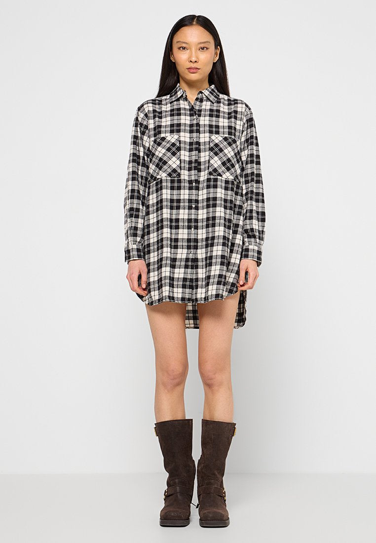 Schwarz-weiße Karobluse mit durchgehender Knopfleiste, langen Ärmeln, Brusttaschen und längerem Rückenteil. Modell trägt braune knielange Stiefel.