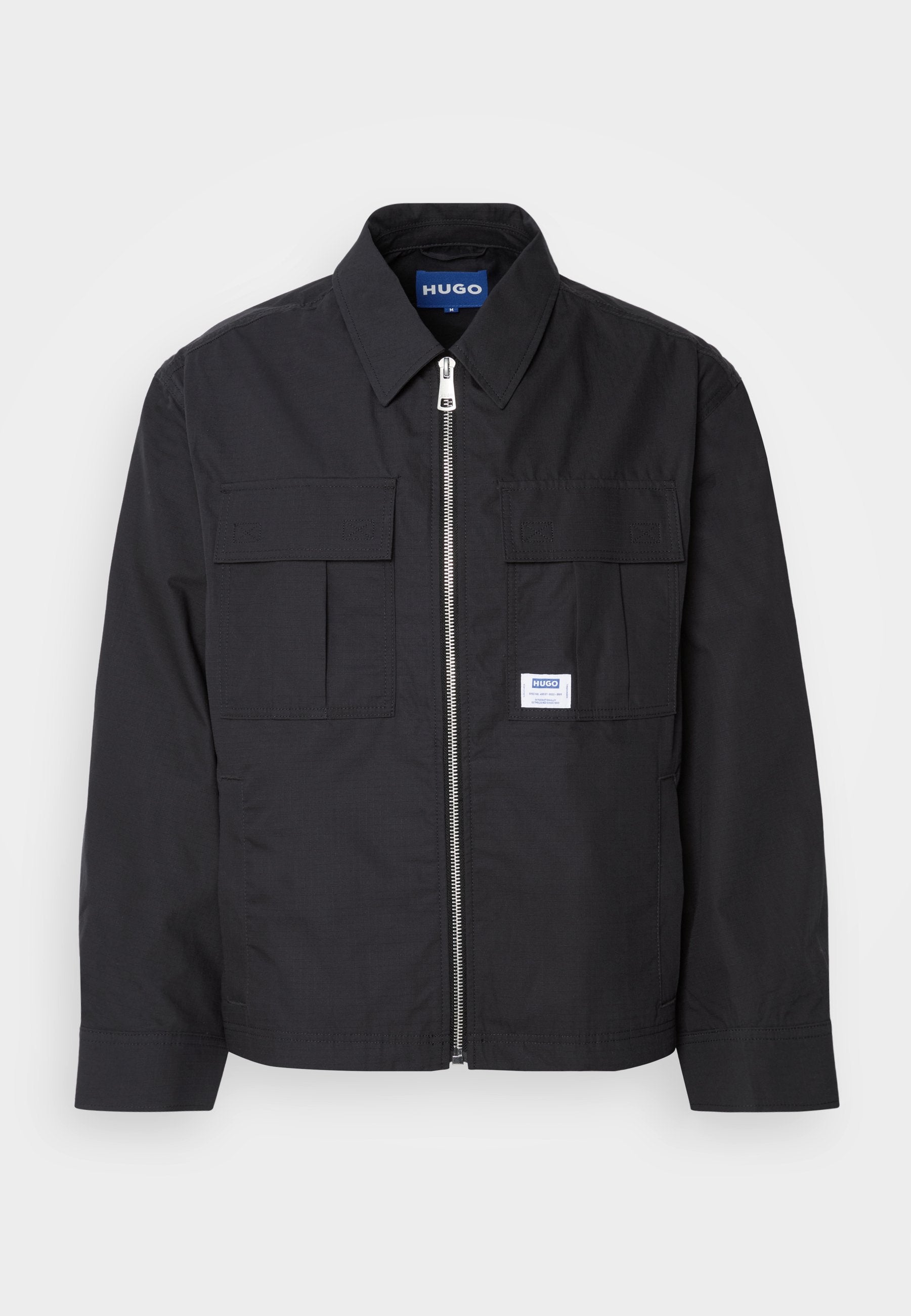 Schwarze Jacke mit Reißverschluss vorne, spitzem Kragen und zwei Brusttaschen. Verfügt über ein gesticktes Logo und strukturiertes Material. Figurbetonter Schnitt mit langen Ärmeln.