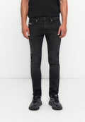 Mann, der eng anliegende schwarze Jeans und schwarze Sportschuhe trägt, steht vor einem weißen Hintergrund, die Hände entspannt an den Seiten.
