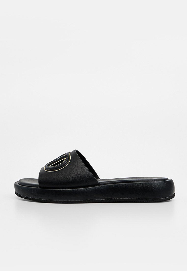 Schwarze Slide-Sandale mit dicker Sohle und breitem Riemen, der im oberen Bereich ein rundes, geprägt Logo zeigt.