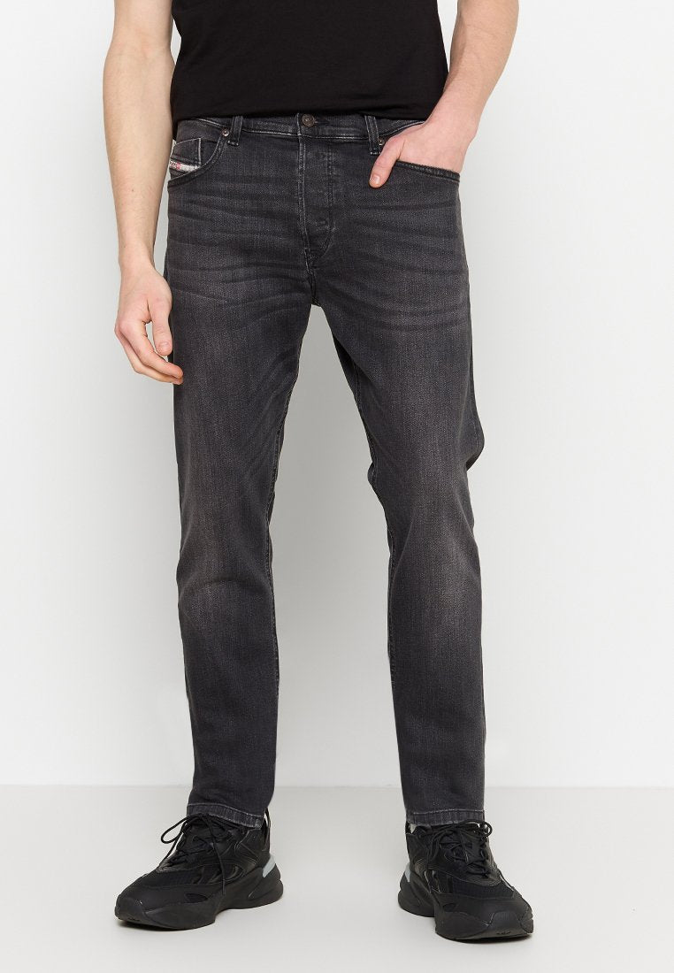 Dunkelgraue Jeans aus Denim mit slim fit, fünf Taschen, dezenten Ausbleichungen und kontrastierenden Nähten. Kombiniert mit schwarzen Sportschuhen.