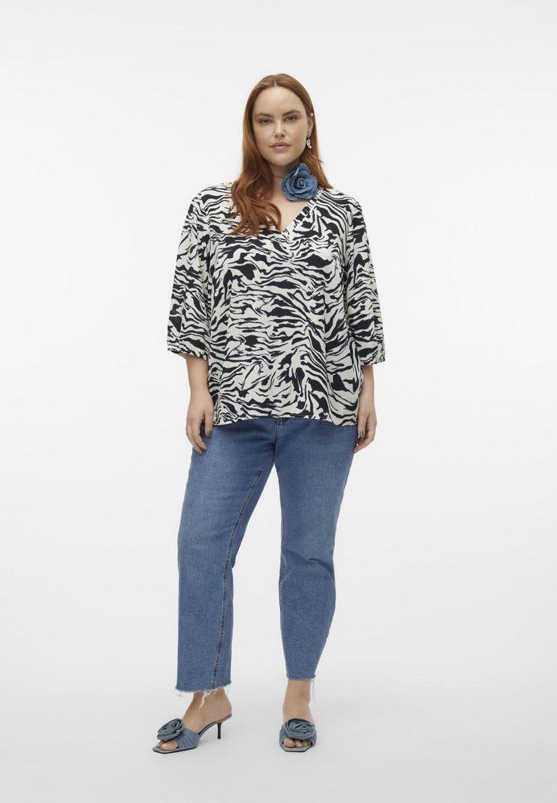 Schwarz-weißer Zebramuster-Top mit V-Ausschnitt und 3/4-Ärmeln, kombiniert mit hellblauen geraden Jeans und passenden blauen Absatzsandalen.