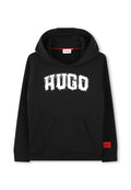 Schwarzer Hoodie aus Baumwollmischung, mit einem roten Logo-Etikett, geräumiger Fronttasche und auffälliger weißer "HUGO"-Schriftzug im Tropf-Style.