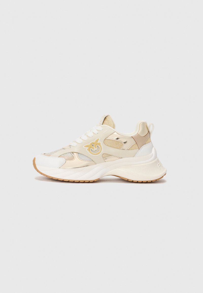 Beige und weiße klobige Sneakers mit Mesh- und Lederpaneelen, weißen Schnürsenkeln, Gummisohle und einem stilisierten gelben Logo an der Seite.