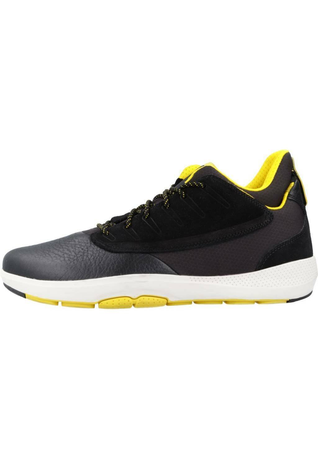 Schwarze und graue Sportschuhe mit einem Obermaterial aus strukturiertem Leder und Mesh, gelben Akzenten und einer weißen Sohle mit sichtbaren Stollen für besseren Halt.