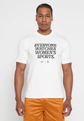 Mann trägt ein weißes T-Shirt mit der Aufschrift "JEDER SCHAUF FRAUENSPORT" und orangefarbene Sportshorts, steht vor einem schlichten Hintergrund.