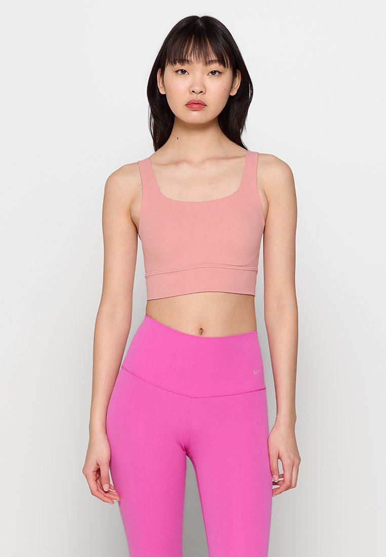 Rosa Sport-BH mit quadratischem Ausschnitt und breiten Trägern, kombiniert mit hochtaillierten rosa Leggings mit einem kleinen Logo. Glatter Stoffeindruck.