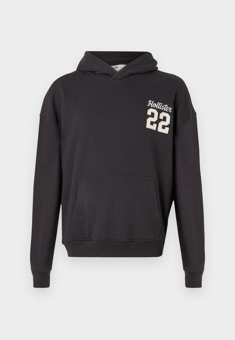 Schwarzer Hoodie mit vorderer Kängurutasche und cremefarbenem "Hollister 22" Logo auf der linken Brust, auf einem schlichten weißen Hintergrund präsentiert.