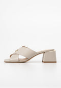 Beige Absatzsandalen mit gekreuzten Riemen, einem goldenen Akzent an einem Riemen, quadratischem Blockabsatz und glattem synthetischem Material.