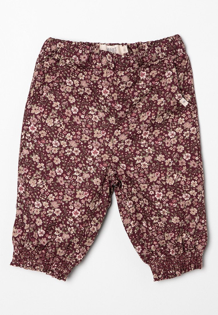 Blumenmusterte, kastanienbraune Hose mit elastischem Bund und Bündchen, die kleine rosa und crèmefarbene Blumen auf einem dunklen Hintergrund zeigt.