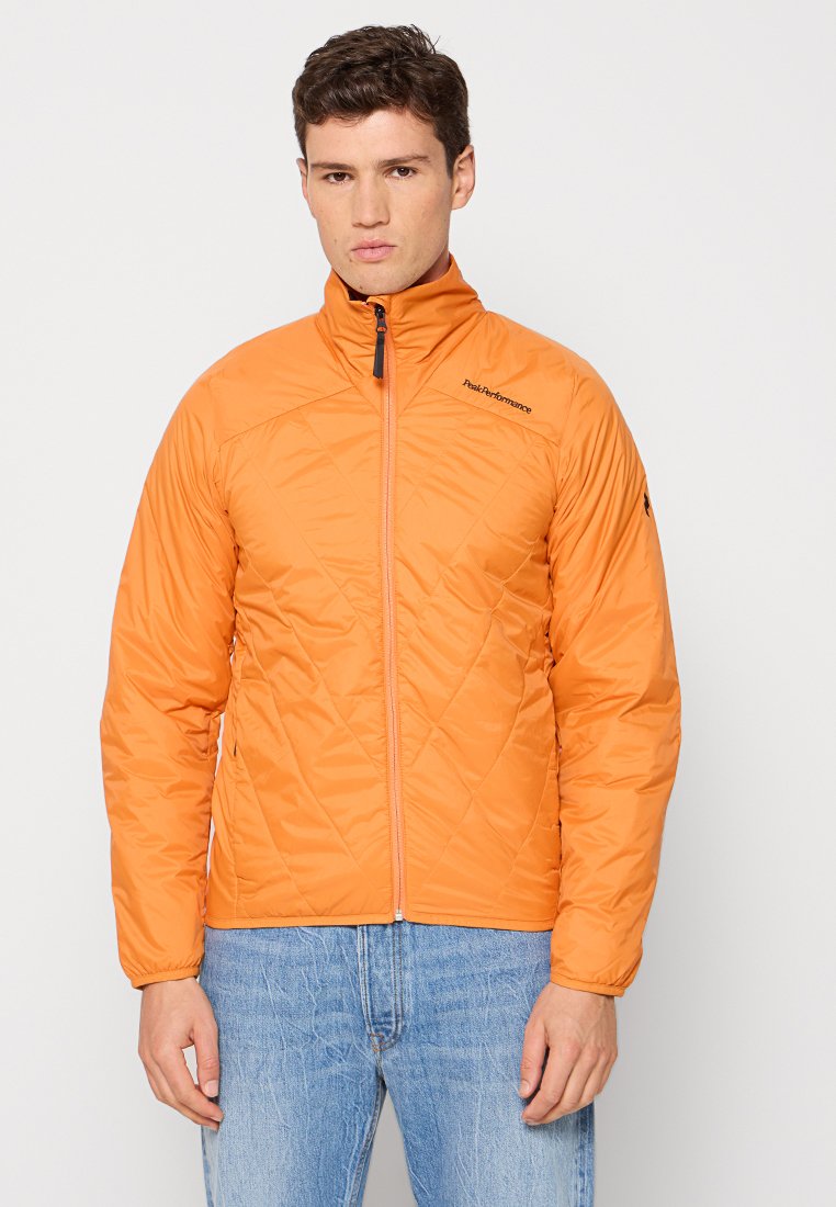 Orangen gesteppte Jacke mit hohem Kragen, durchgehendem Reißverschluss vorne und einem Logo auf der linken Schulter. Kombiniert mit hellblauen Jeans.