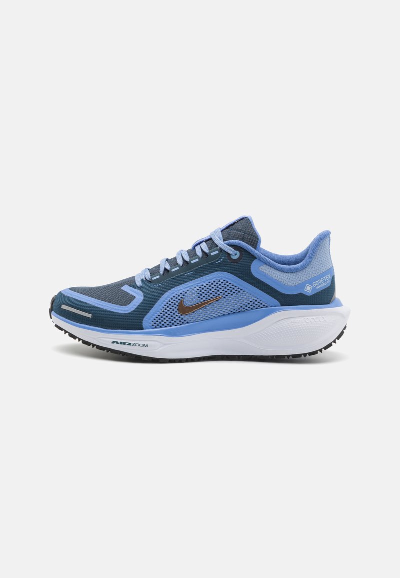 Blaues und marineblaues Laufschuh mit Netzobermaterial, silbernen Akzenten und weißer Sohle. Verfügt über eine strukturierte Oberfläche und ein auffälliges Nike-Logo.