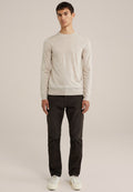 Helle beige Langarmpullover mit Rundhalsausschnitt, strukturierter Stoff. Getragen mit dunklen Hosen und weißen Sneakers. Modell steht, neutraler Hintergrund.