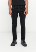 Mann, der vor einem weißen Hintergrund steht, trägt schmale schwarze Jeans und schwarz-graue Sportschuhe, die Hände entspannt an den Seiten.