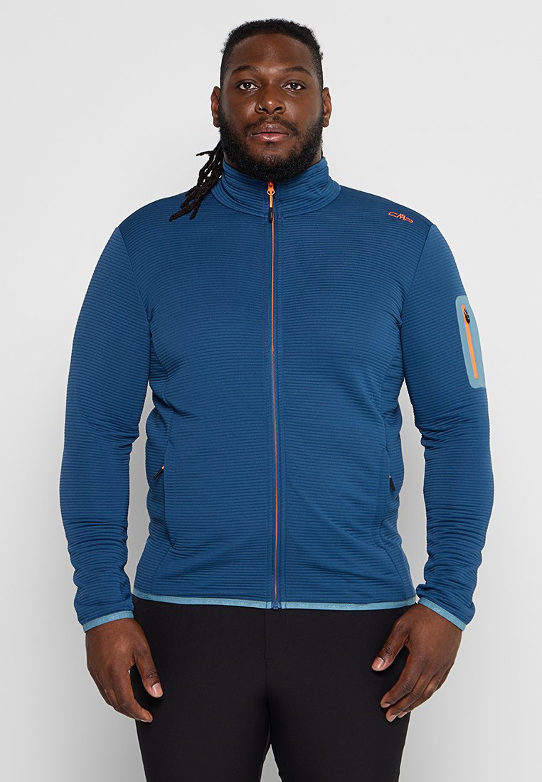 Blauer Reißverschlussjacke mit horizontaler Rippstruktur, orangefarbenem Reißverschluss, Taschen an den Seiten und einer Tasche am Oberarm mit einem orangefarbenen Akzent.