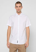 Weißes kurzärmeliges Hemd mit Button-Down-Kragen, versehen mit einer Frontblende und einer strukturierten Oberfläche. Kombiniert mit hellbraunen Hosen.