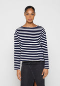 Frau trägt ein marineblau-weiß horizontal gestreiftes Langarmshirt und einen dunkelgrauen, hoch taillierten Rock mit Frontschlitz.
