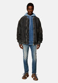 Männliches Model trägt eine übergroße schwarze Jeansjacke, einen blauen Kapuzenpullover, verwaschene Slim-Fit-Jeans und mehrfarbige Schnürsneaker und steht aufrecht.