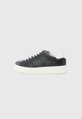 Schwarzer niedriger Sneaker mit weißen Schnürsenkeln, weißer Sohle und weißem Fersenlasche, im Seitenprofil vor einem hellgrauen Hintergrund gezeigt.