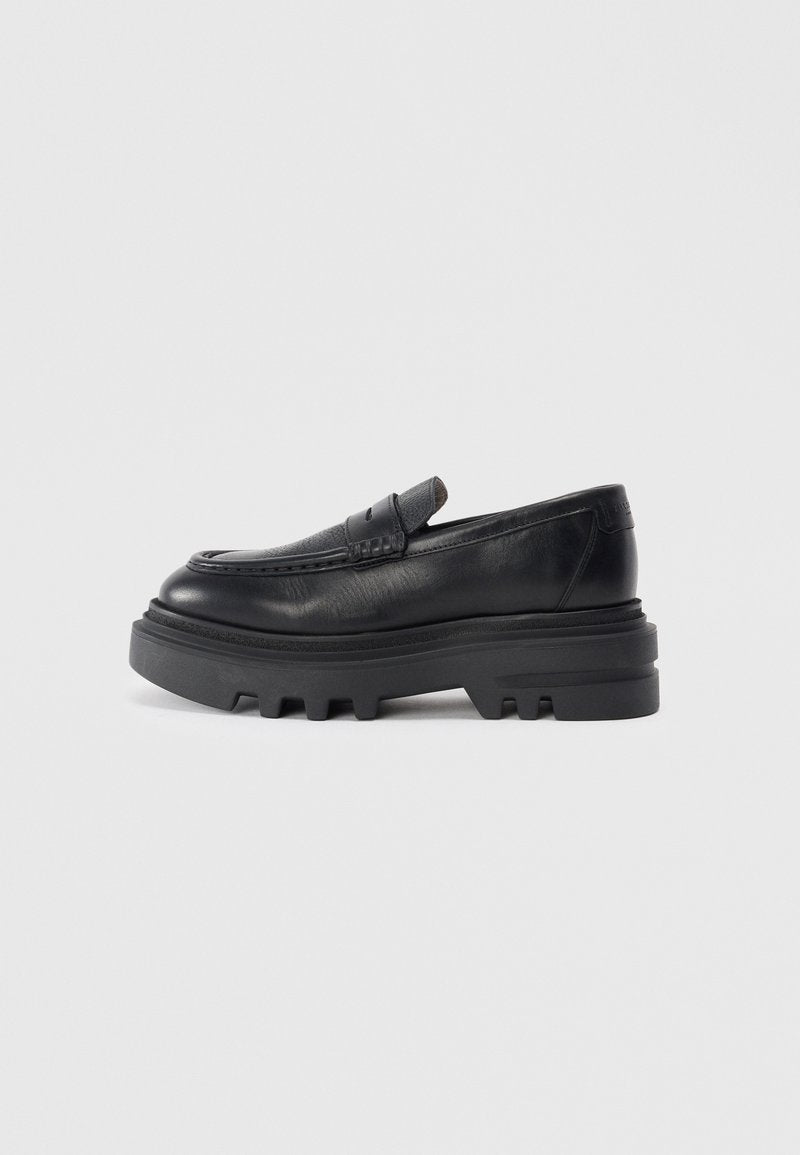 Schwarzer Lederloafer mit dicker schwarzer Sohle und strukturiertem Riemendetail. Die glatte Oberfläche und die runde Form betonen das zeitgenössische Design.