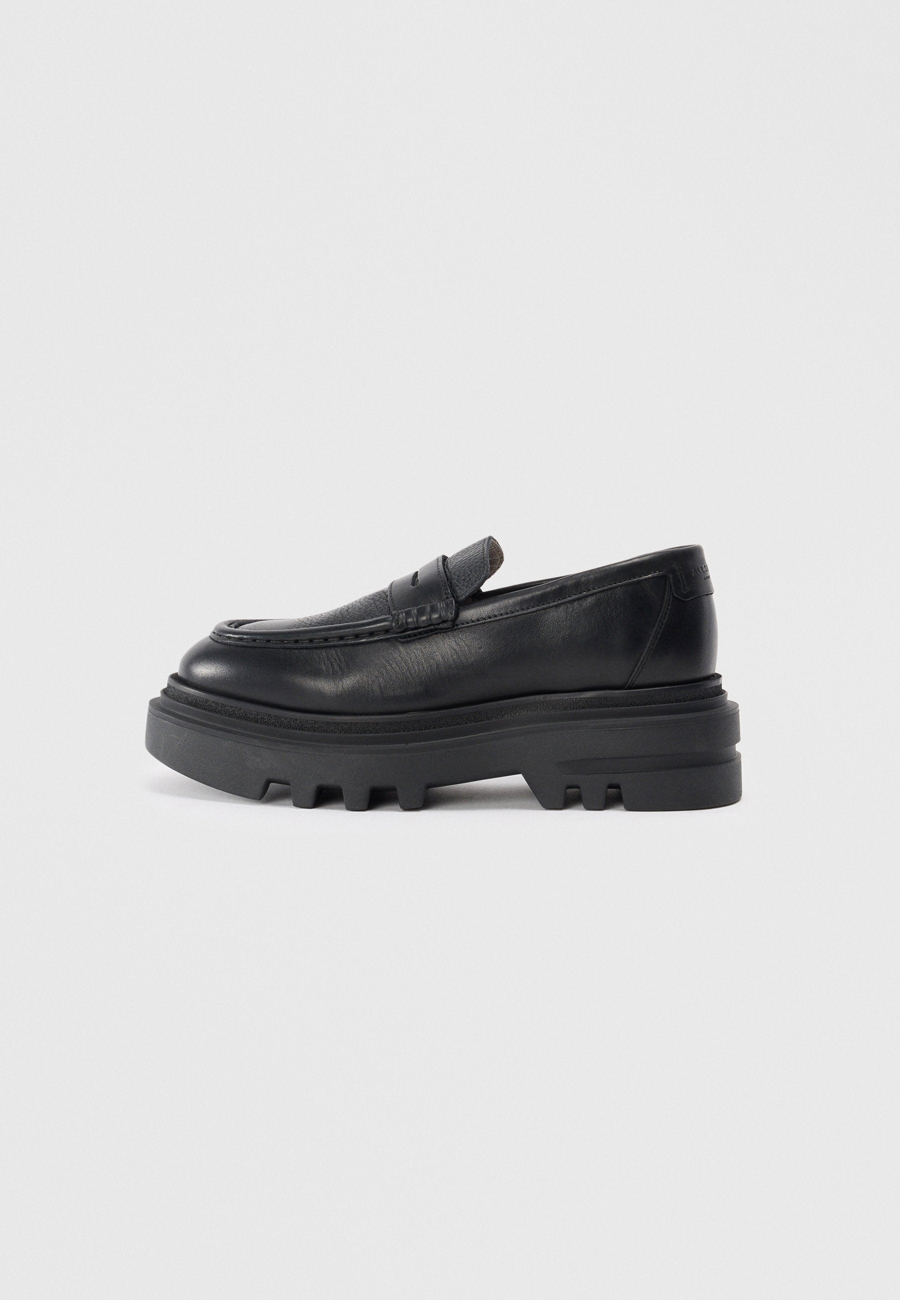 Schwarzer Lederloafer mit dicker schwarzer Sohle und strukturiertem Riemendetail. Die glatte Oberfläche und die runde Form betonen das zeitgenössische Design.