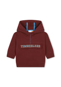 Burgunderfarbene Kapuzenjacke mit halbem Reißverschluss, einer Kängurutasche und blauem "TIMBERLAND"-Logo auf der Brust. Weicher Stoff, gerippte Bündchen.