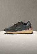 Sneakers bestehen aus einer Kombination von dunkelgrünem und grauem Wildleder, mit orangen Schnürsenkeln, einem gut sichtbaren Logo und einem mehrfarbigen, gestreiften Fersen-Akzent.