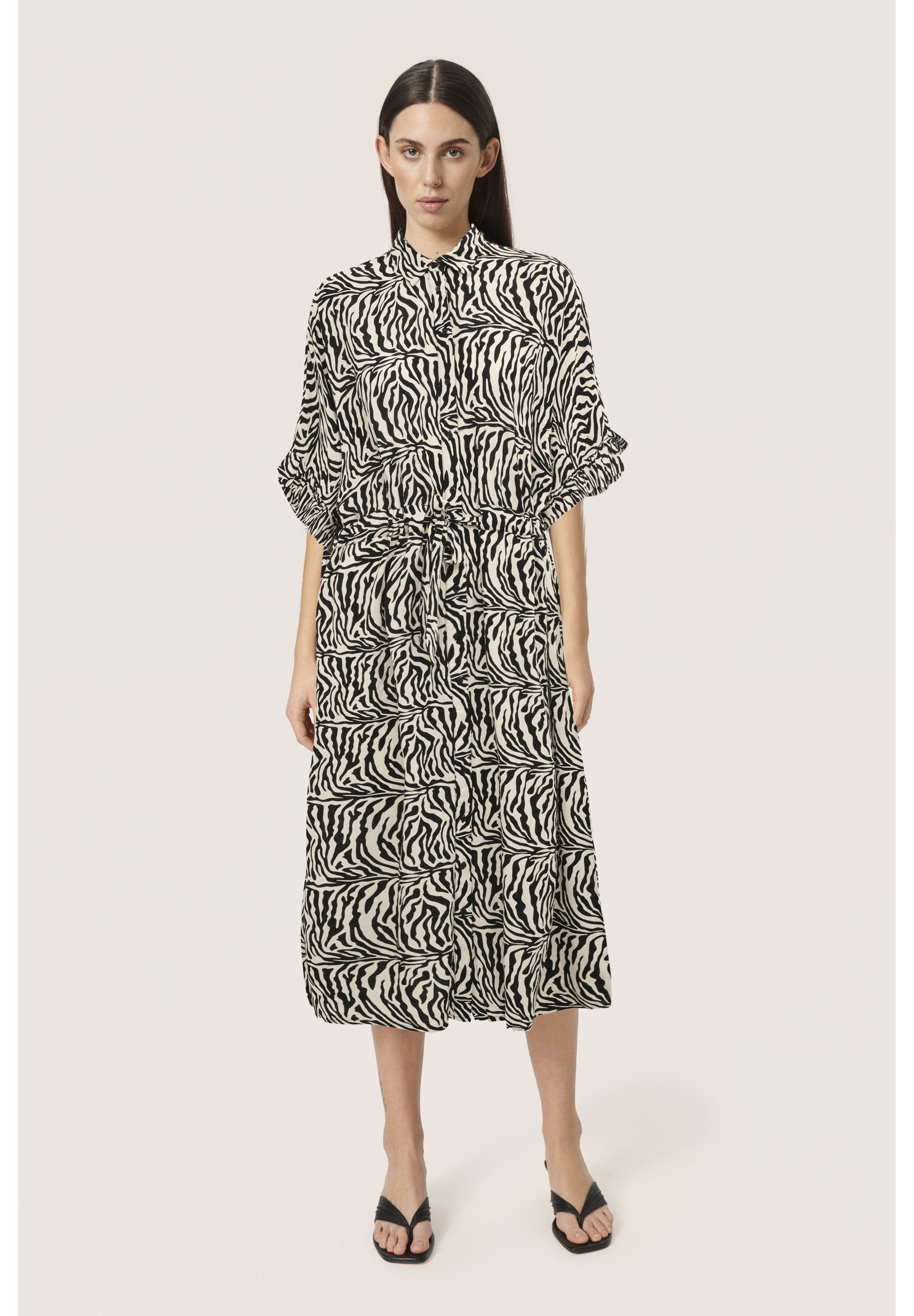 Schwarz-weißes Kleid im Zebra-Muster mit Kragen, kurzen Ärmeln und elastischem Bund. Fließender Stoff, knielanges Design.