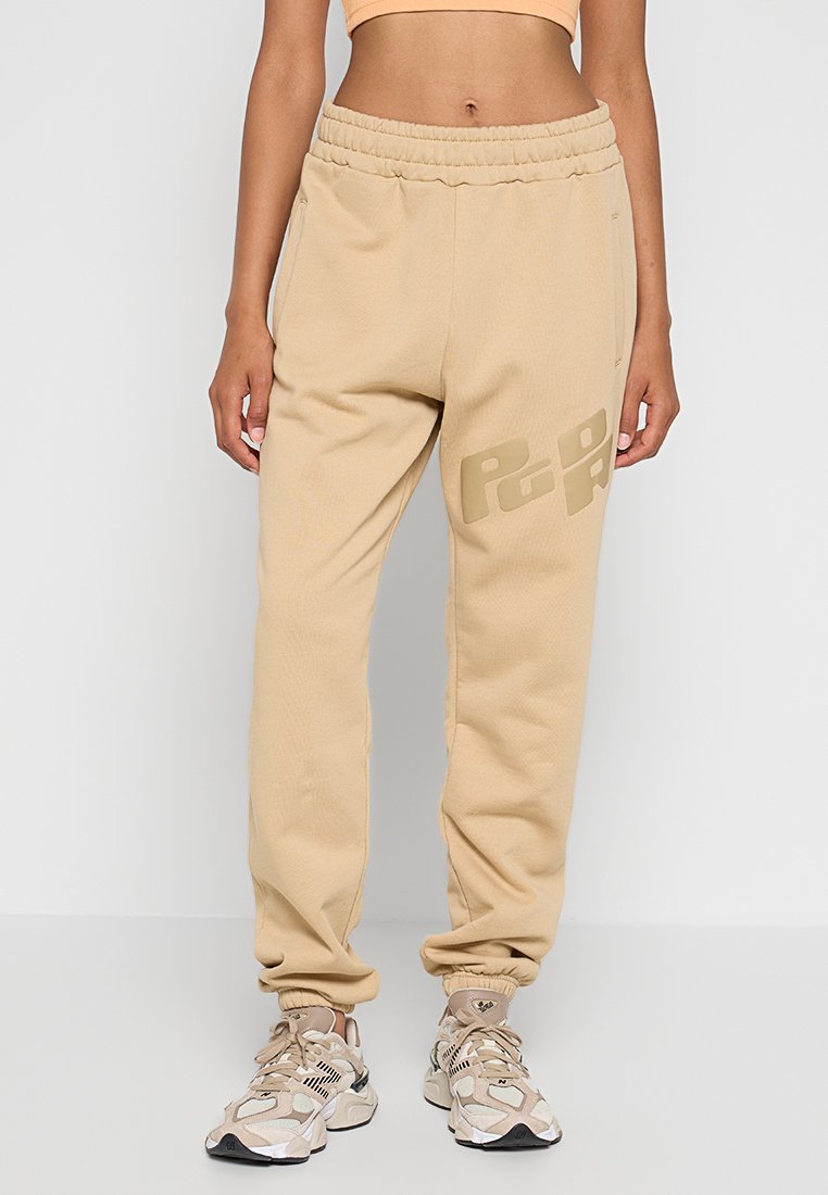 Beige Fleece-Jogginghosen mit gerippten Knöchelen, elastischem Bund, Seitentaschen und auffälligem Logo in einer dunkleren Nuance am Oberschenkel.
