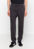 Mann in schwarzen Sweatpants mit Zugband und dem Schriftzug "New York City" an der Seite, sowie schwarzen Turnschuhen mit weißen Streifen, steht auf einem weißen Boden.