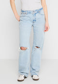 Hellblaue, ausgewaschene Denim-Jeans mit weit geschnittenen Beinen, die auffällige Rissdetails an den Knien und fransige Kanten aufweisen. Getragen mit weißen Sneakers.