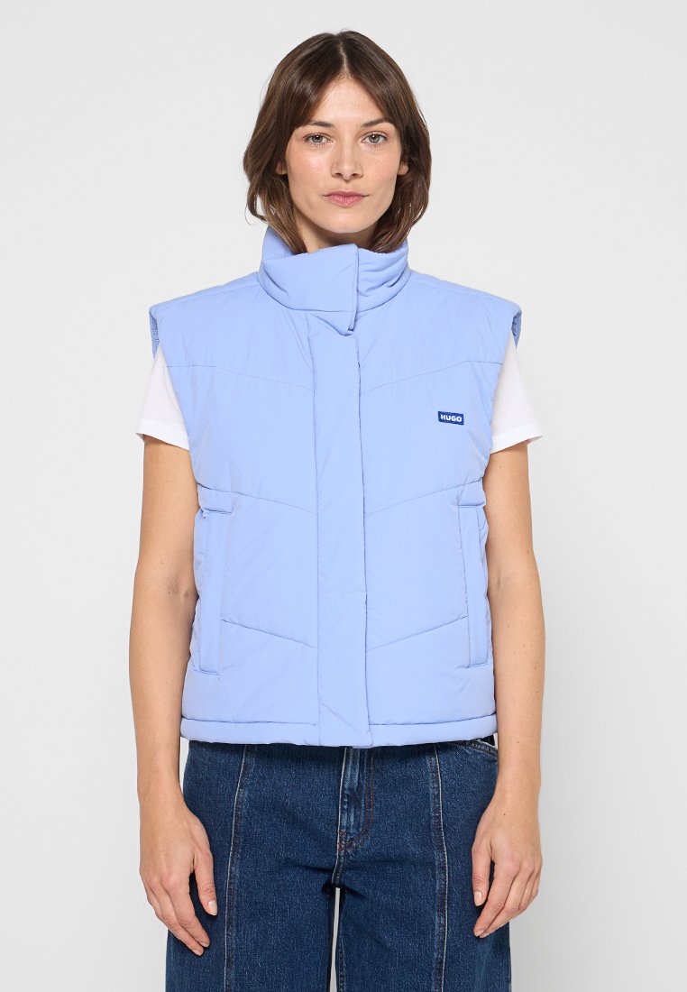 Hellblaue Steppweste mit hohem Kragen, Reißverschluss und zwei Fronttaschen; zeichnet sich durch ein gestepptes Panel-Design und einen Logo-Patch auf der Brust aus.