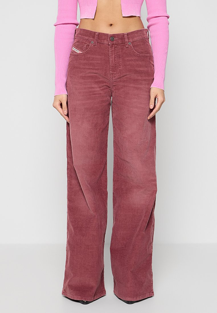 Weite Cordhosen in staubigem Rosa mit hoher Taille, frontalen Taschen und subtiler Textur. Kombiniert mit einem figurbetonten rosa Oberteil.