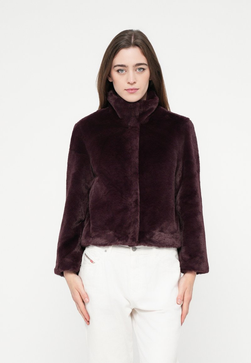 Kurze lila Kunstpelzjacke mit hohem Kragen und kurzer Passform. Glatte Textur und lange Ärmel. Kombiniert mit weißen Hosen.