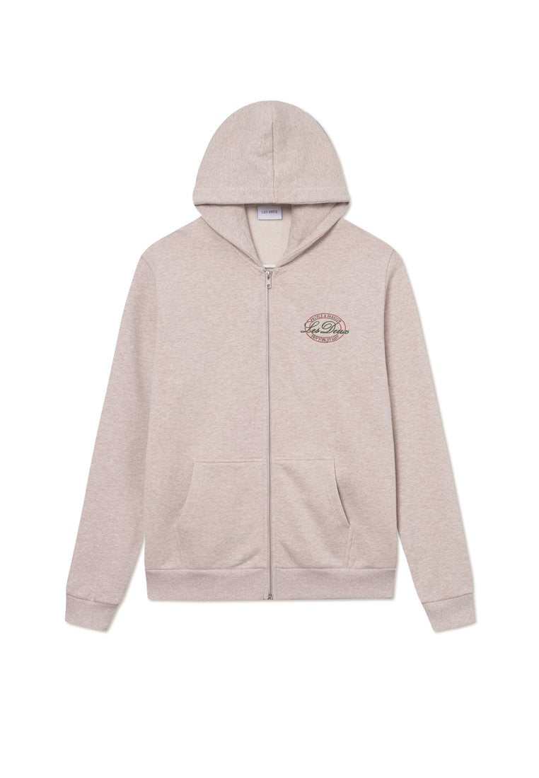Hellbeige Zip-Hoodie mit Kordelzugkapuze, zwei vorderen Taschen und einem runden Logo auf der linken Brustseite. Material aus Baumwollmischung.
