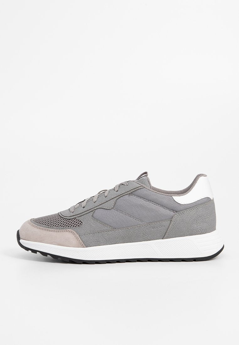 Grauer Sportschuh mit einem Obermaterial aus Mesh und Wildlederelementen, einer weißen Fersenabdeckung und einer strukturierten Gummisohle. Elegantes, leichtes Design.