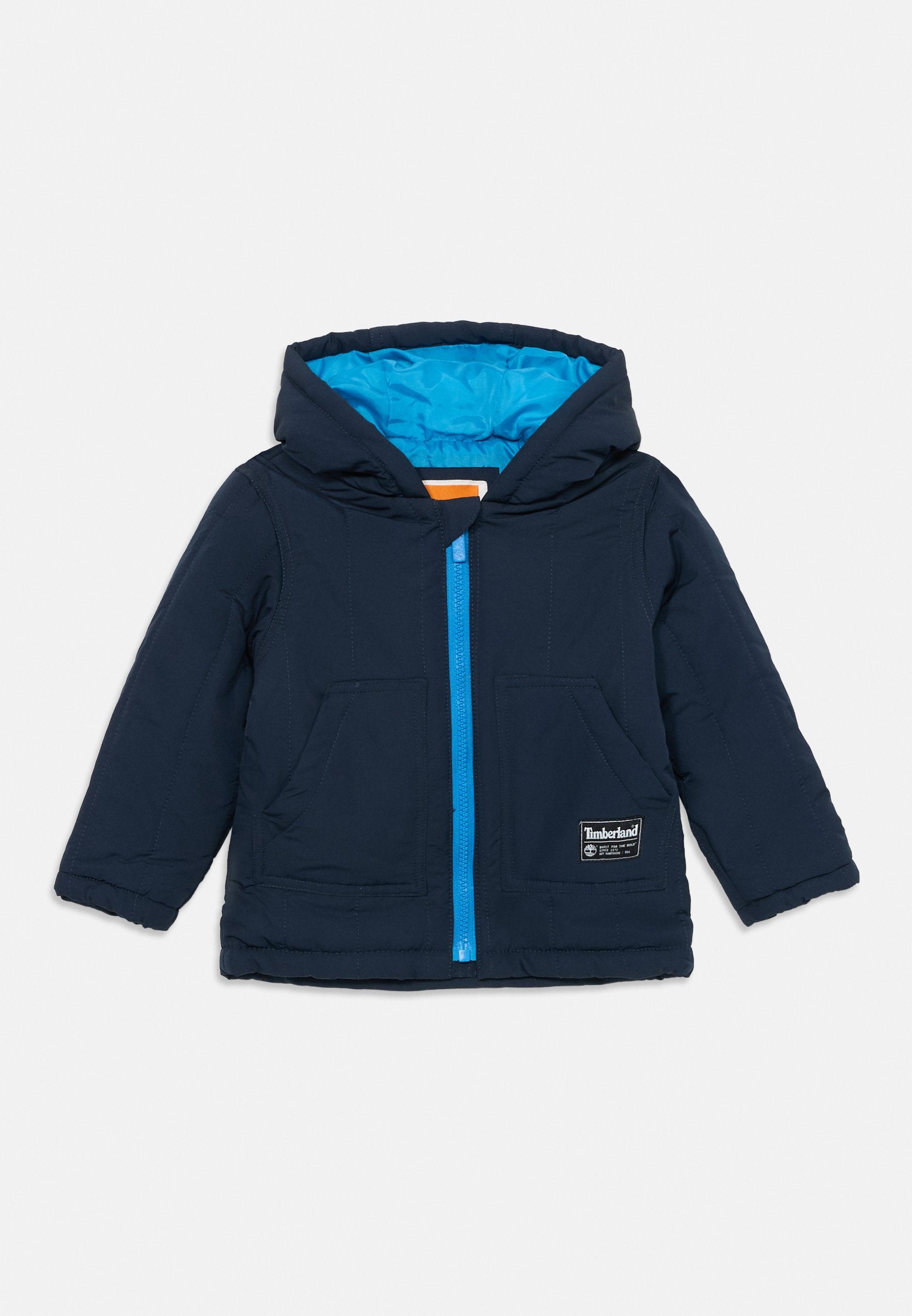 Marineblaue Steppjacke mit blauer Innenauskleidung, Reißverschluss vorne, zwei Fronttaschen und Kapuze. Mit einem Timberland-Logo an der Unterseite.