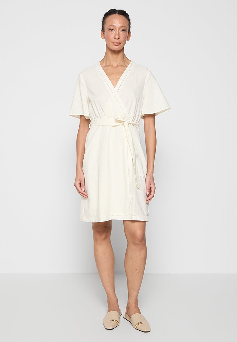 Cremefarbiges Wickelkleid mit kurzen, ausgestellten Ärmeln und einem Bindegürtel, das einen V-Ausschnitt und eine lockere Passform bietet. Glatte Stoffoberfläche.
