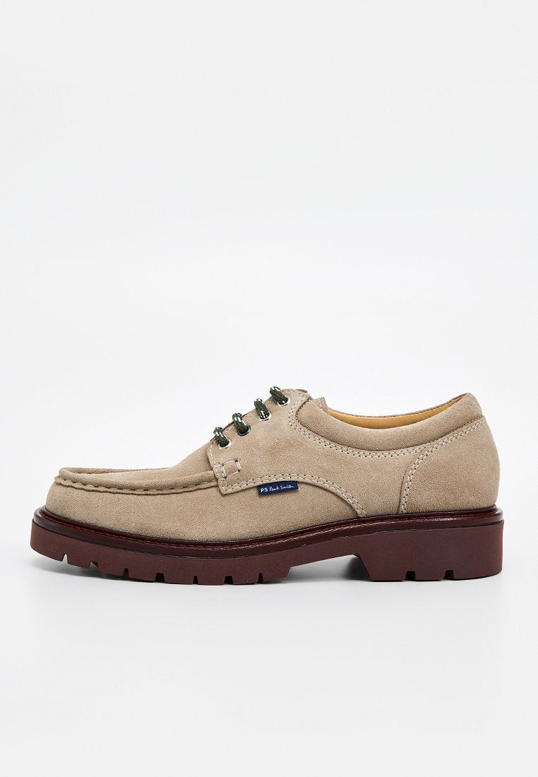 Beiger Wildlederschuh mit abgerundeter Spitze, drei Ösen zum Schnüren, grünen Schnürsenkeln und brauner Gummisohle mit detailliertem Profil. Blaues Markenetikett an der Seite.