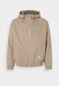 Helle beige Kapuzenjacke aus glattem Stoff mit einem Frontreißverschluss, elastischem Saum und grünem Logo-Akzent auf der unteren rechten Seite.