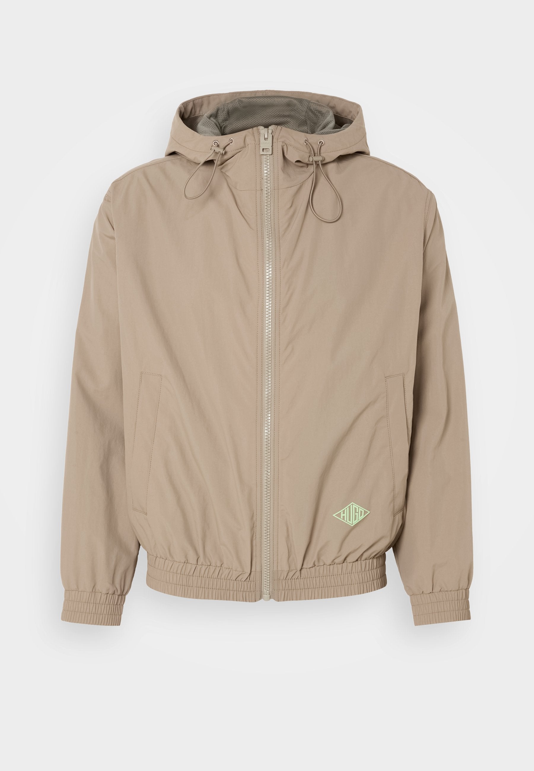 Helle beige Kapuzenjacke aus glattem Stoff mit einem Frontreißverschluss, elastischem Saum und grünem Logo-Akzent auf der unteren rechten Seite.