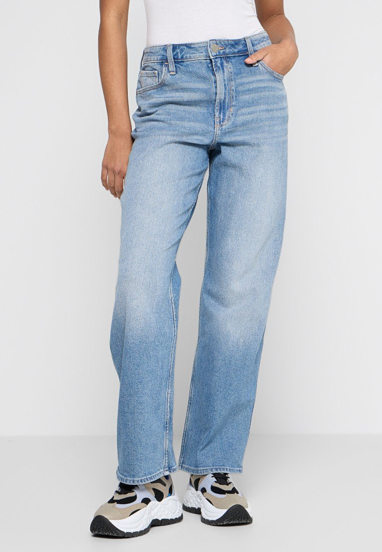Helle blaue weit geschnittene Jeans aus Denim mit hoher Taille, geradem Schnitt und minimalen Used-Effekten. Kombiniert mit mehrfarbigen Sneakers.