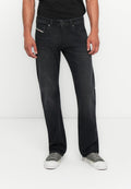 Dunkelblaue Denim-Jeans mit geradem Schnitt, subtiler Textur und vorderen Taschen. Getragen mit grauen Sneakers und einem schwarzen Shirt.
