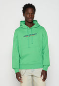 Junger Mann mit einem leuchtend grünen Hoodie mit dem Text "Diesel Industry Denim Division" und hellbeigen Jeans mit einer silbernen Kette.