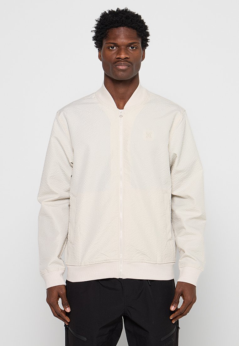 Hellbeige Bomberjacke mit strukturiertem Muster, Frontreißverschluss und gerippten Bündchen, mit einem dezenten auf der Brust bestickten Logo.