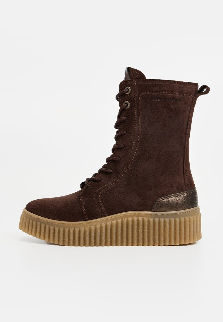 Braune Wildleder-Stiefeletten mit einer strukturierten Plateausohle, Metallösen und einem metallischen Akzent an der Ferse. Die Schnürsenkel reichen bis zur Mitte der Höhe.