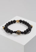Armband aus schwarzem Lavastein mit einer goldfarbenen Verschluss- und Akzentfarbe. Verfügt über ein geflochtenes Band und einen dekorativen Charme in der Mitte.